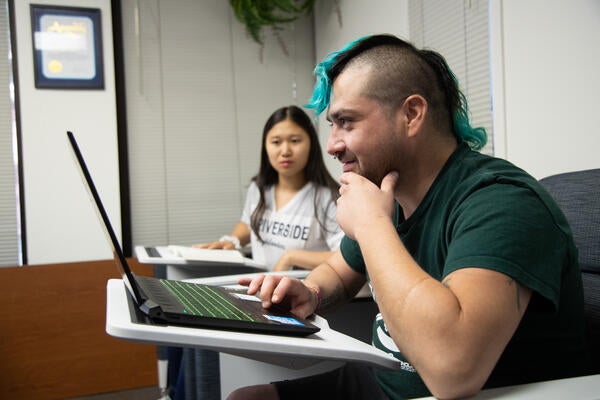 A student looks intently at their laptop screen along side a fellow student. 