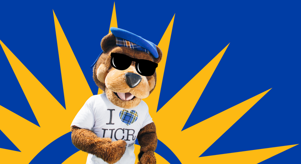 UCR's mascot Scotty wears sunglasses, a blue beret, and an I heart UCR tshirt while standing in front of an illustration of the sun