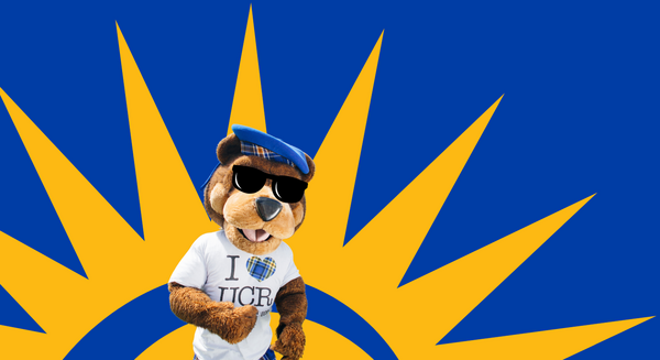 UCR's mascot Scotty wears sunglasses, a blue beret, and an I heart UCR tshirt while standing in front of an illustration of the sun